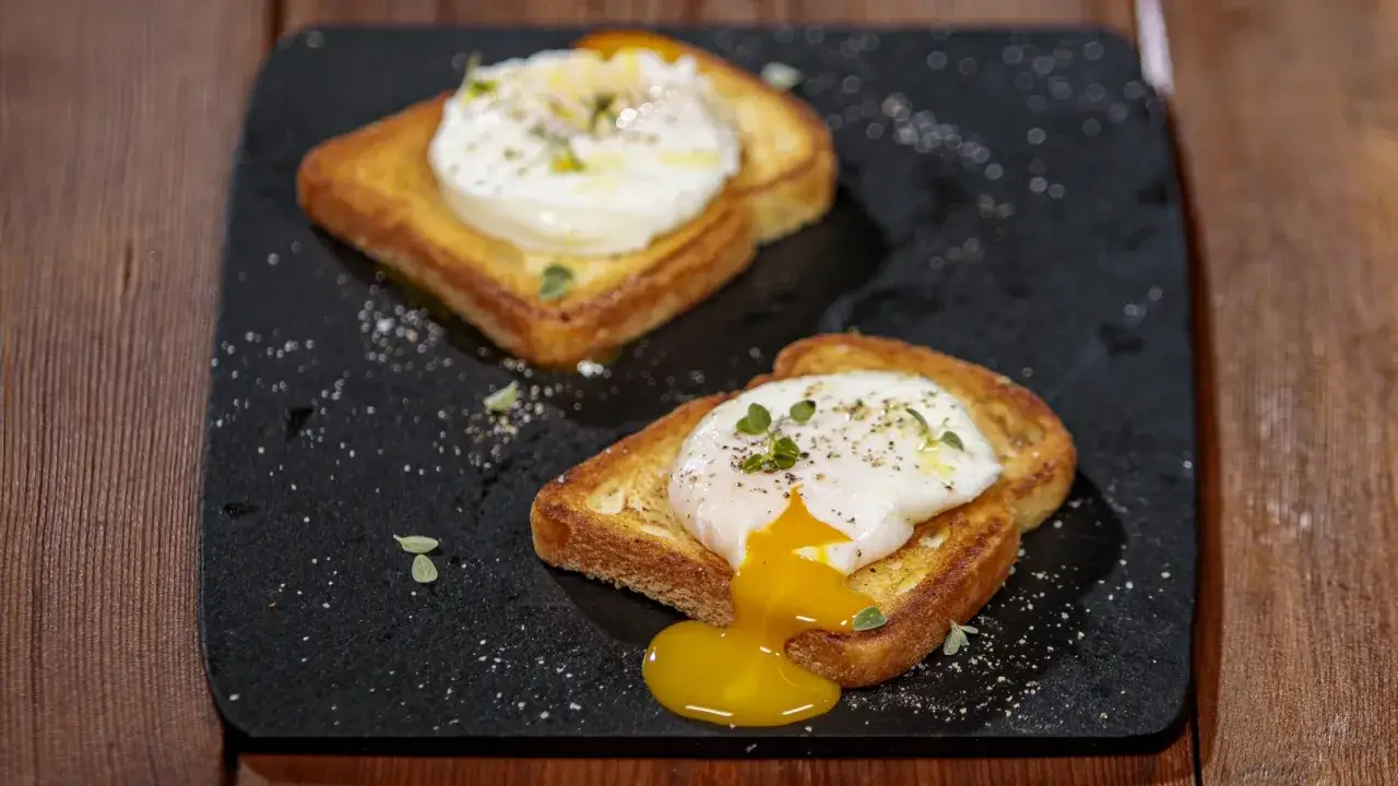 Due fette di pane tostato con un uovo in camicia, guarnite con erbe aromatiche e pepe. Il tuorlo di un uovo cola golosamente.