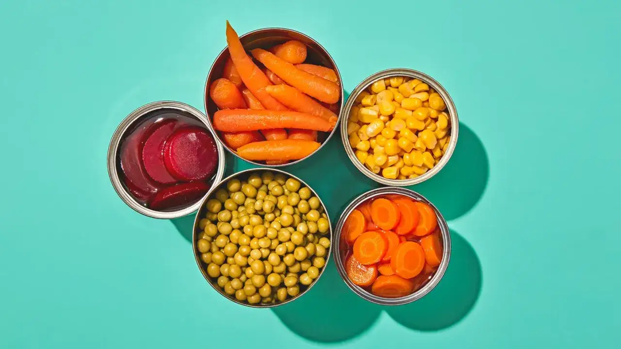 Barattoli aperti con carote, piselli, mais, barbabietole e carote a rondelle. Alcuni di questi potrebbero essere tra i 20 alimenti che alzano la pressione.