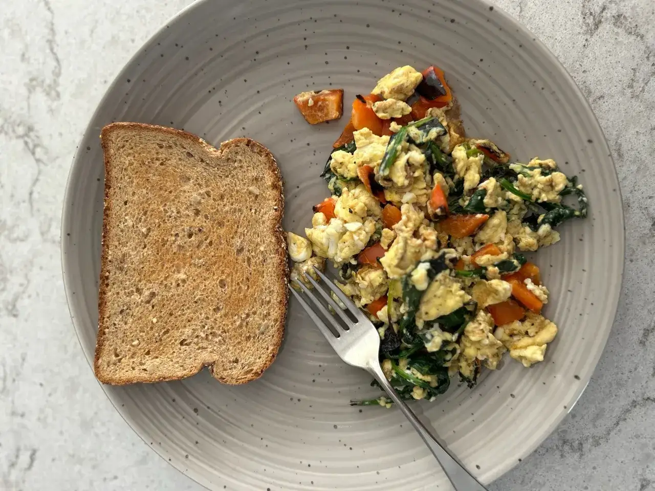 Colazione con uova strapazzate, spinaci, carote e pane tostato. Quante uova a settimana per un pasto così nutriente?
