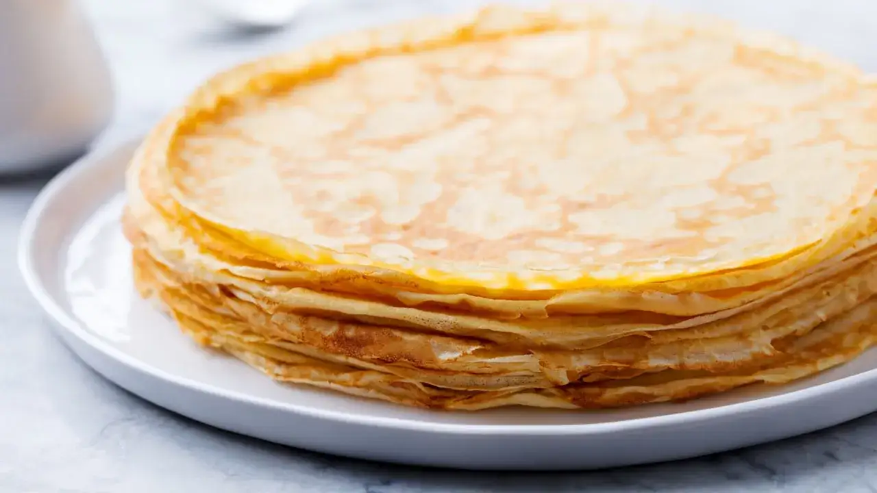 Pila di crepes dorate su un piatto bianco, perfette per una crepes ricetta senza burro.