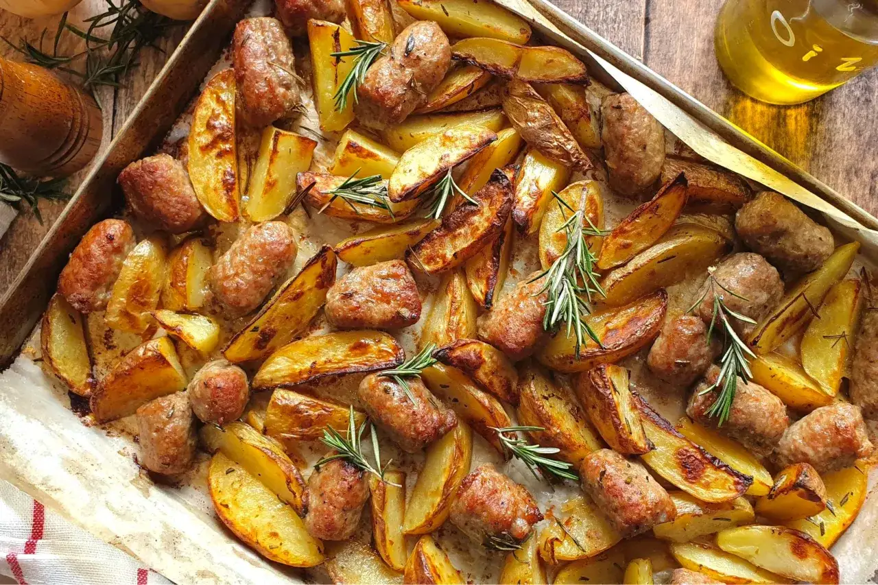 Salsiccia e patate al forno, dorate e profumate al rosmarino, su una teglia. Un piatto rustico e invitante.