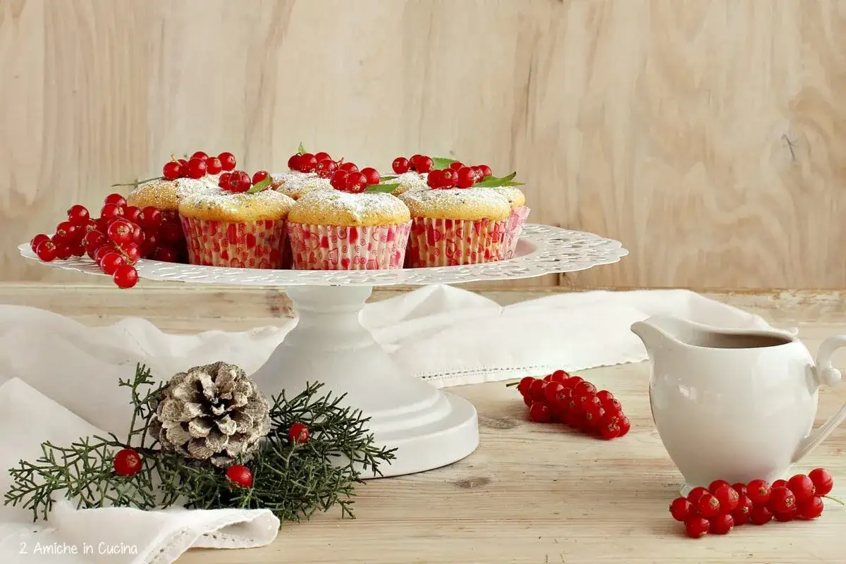 Muffin decorati con zucchero a velo e un generoso topping frutti di bosco, su un'alzata bianca.