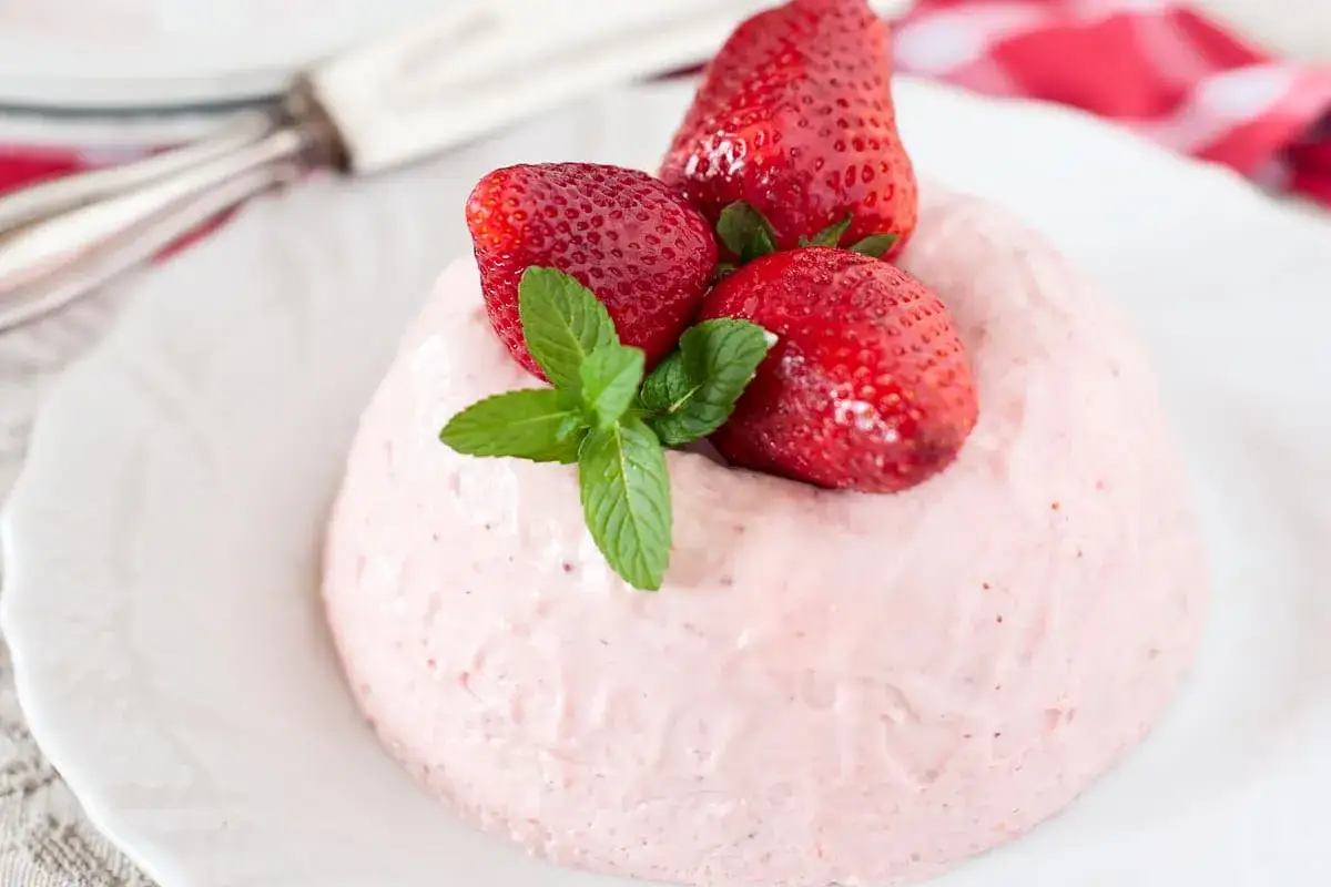 Delizioso bavarese alle fragole, guarnito con fragole fresche e menta, su un piatto bianco.