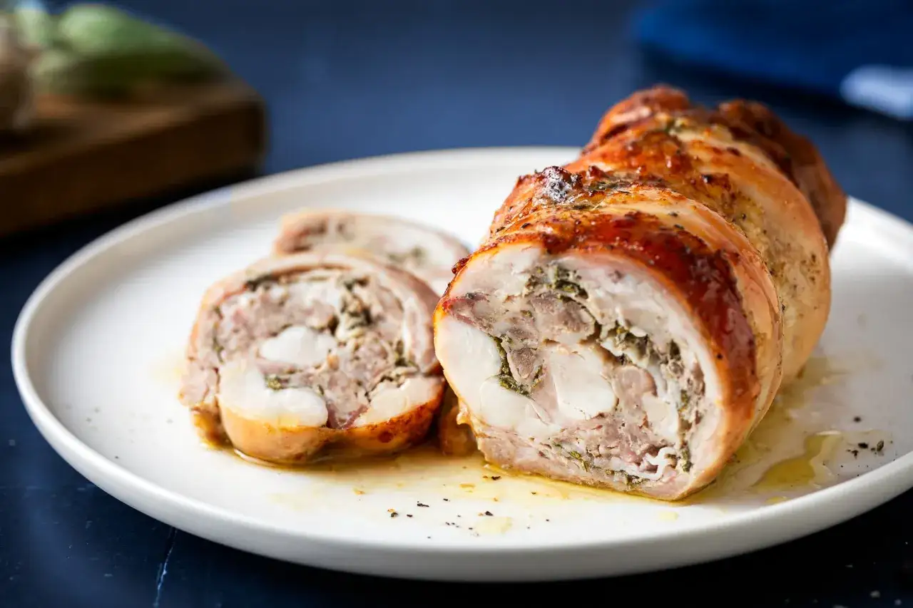 Coniglio in porchetta, un rotolo di carne succulento e aromatico, servito su un piatto bianco con fette tagliate.
