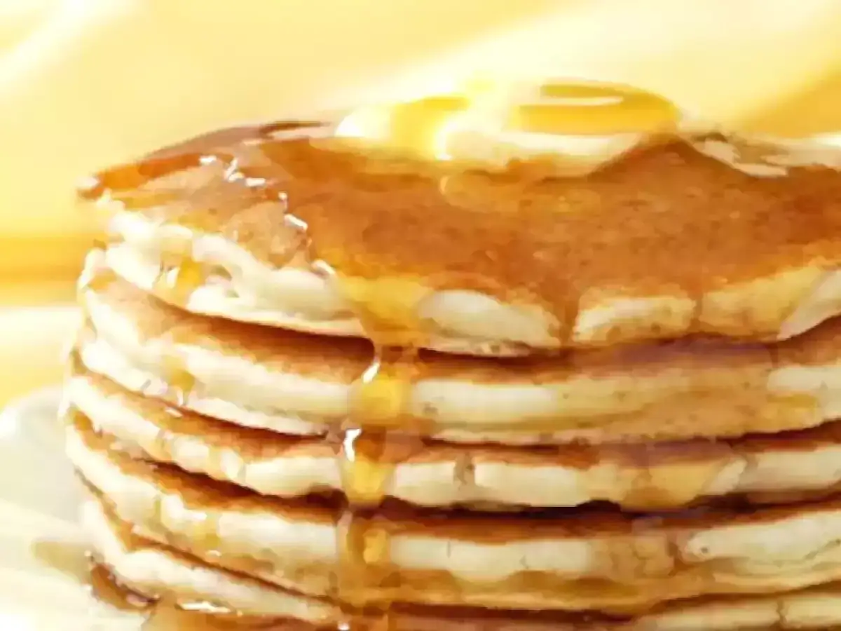 Una pila di soffici pancake senza glutine, ricoperti di sciroppo dorato e una noce di burro che si scioglie.