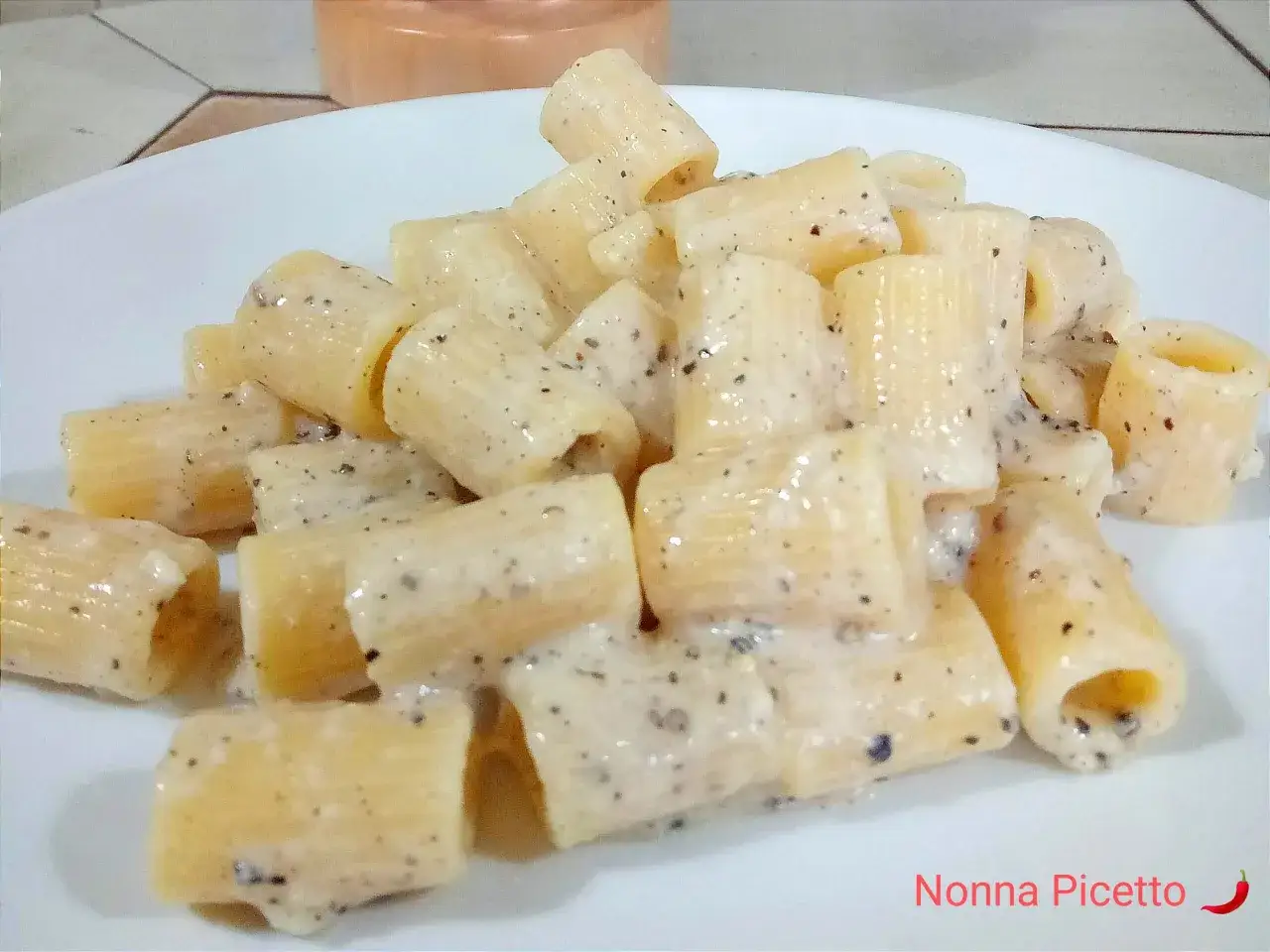 Un piatto di rigatoni cremosi conditi con un classico cacio e pepe, pronti per essere gustati.