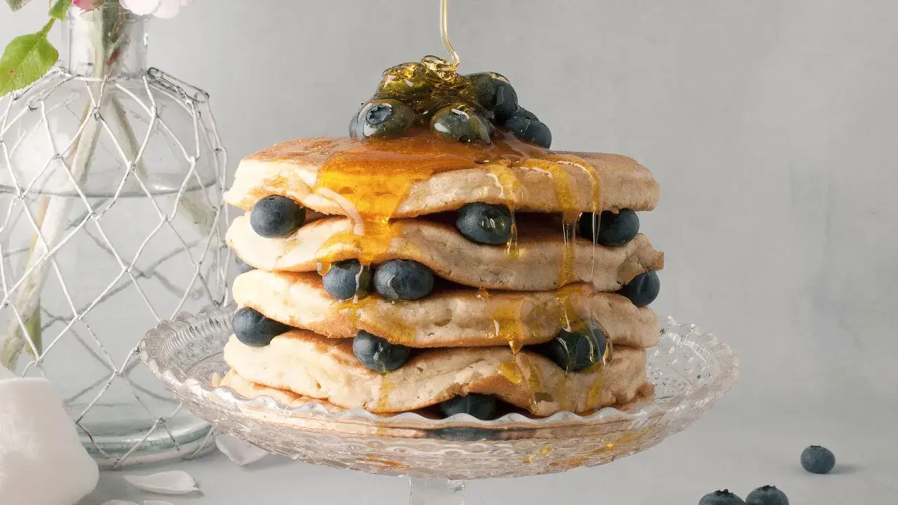 Pancake senza latte, una torre dorata con mirtilli freschi e sciroppo d'acero che cola. Delizioso e leggero!
