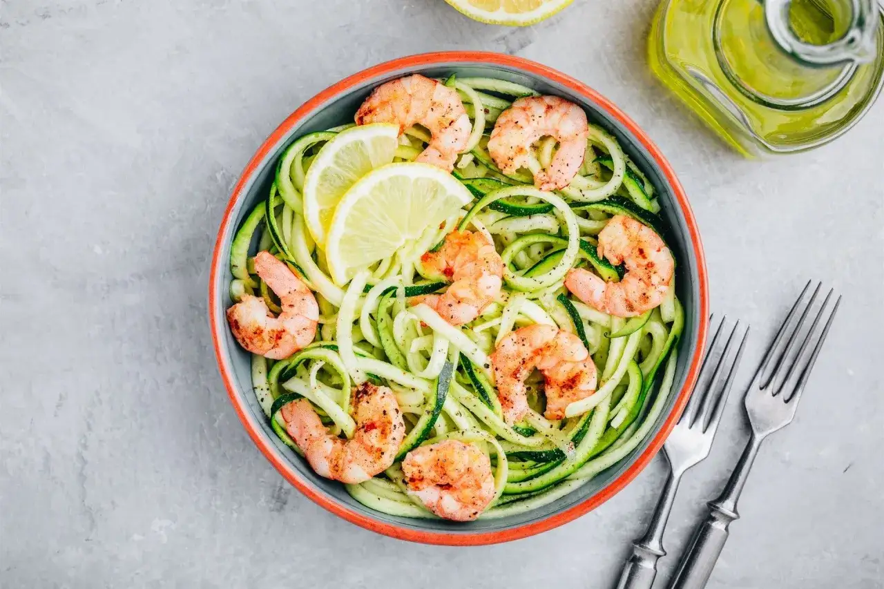 Gamberetti saltati su spaghetti di zucchine, guarniti con limone. Un modo semplice per imparare come cuocere i gamberetti surgelati.