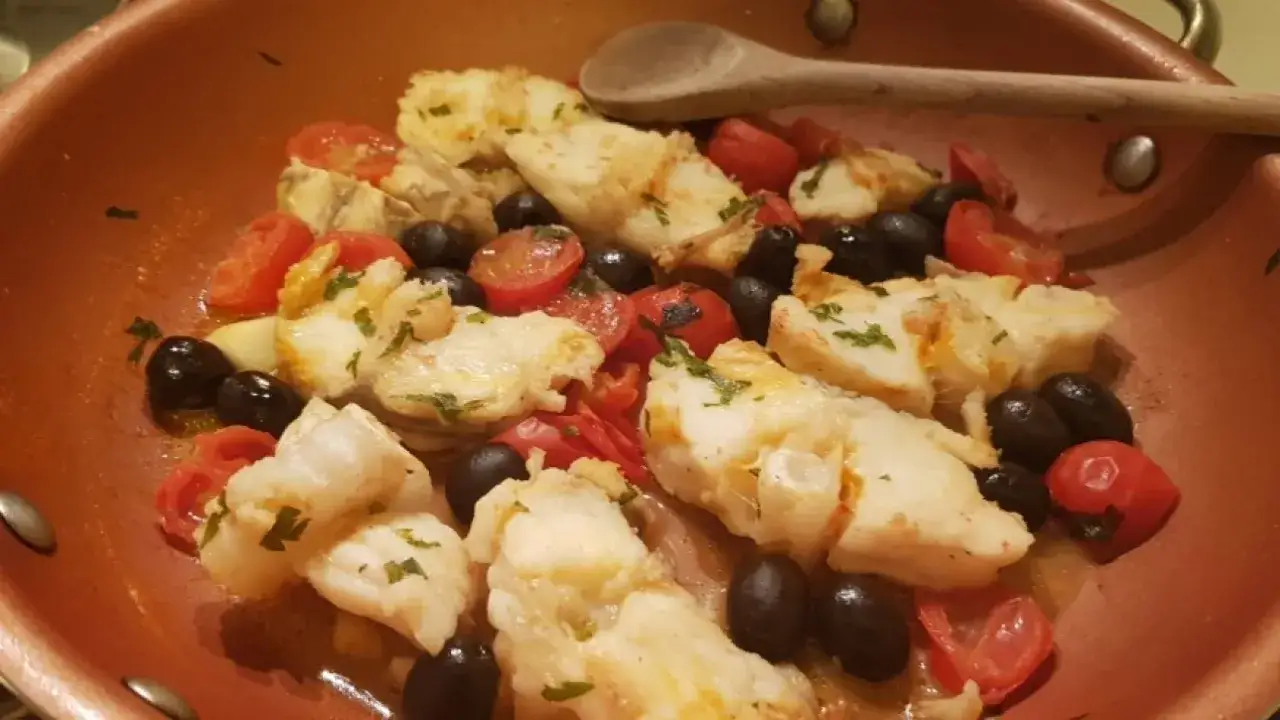 Coda di rospo cotta in padella con pomodorini e olive nere, un piatto saporito e colorato.
