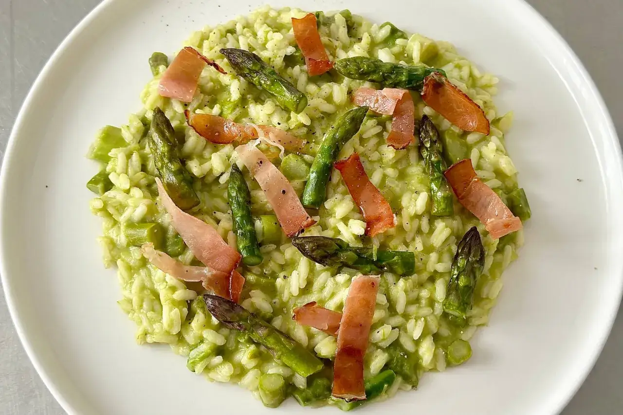Risotto cremoso con asparagi freschi e croccanti striscioline di speck, un piatto primaverile da gustare.