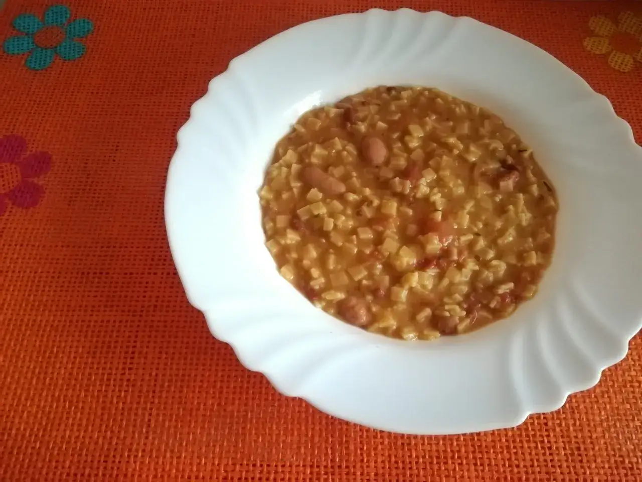 Un piatto di pasta e fagioli in scatola, un pasto veloce e gustoso, servito su una tovaglietta arancione con fiori.