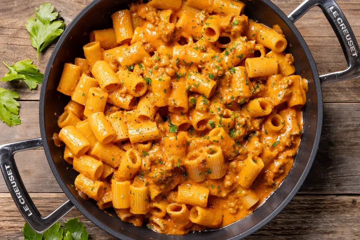 Un pentolone pieno di pasta mezze maniche cremosa con ragù e prezzemolo tritato, pronta per essere gustata.