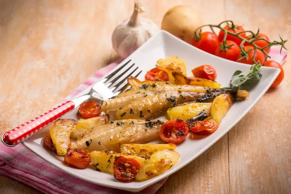 Deliziosa coda di rospo al forno con patate e pomodorini, guarnita con erbe aromatiche.