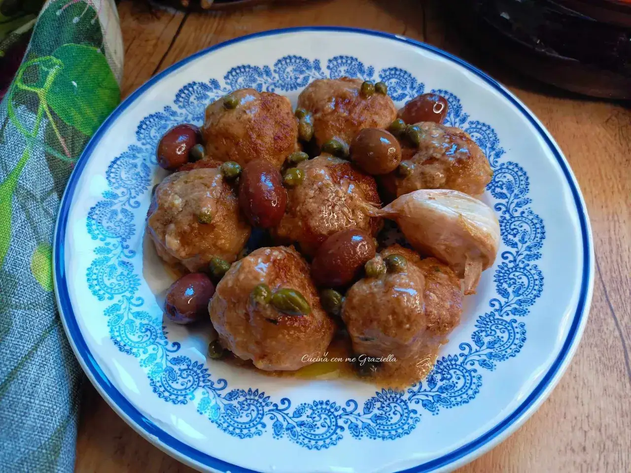 Polpette in bianco su piatto decorato, con olive, capperi e aglio. Un piatto gustoso e invitante.