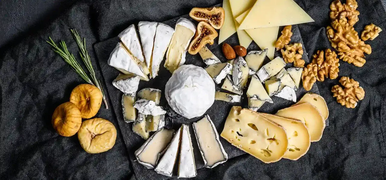 Assortimento di diversi tipi di formaggio, fichi secchi, noci e rosmarino su una tavola scura.