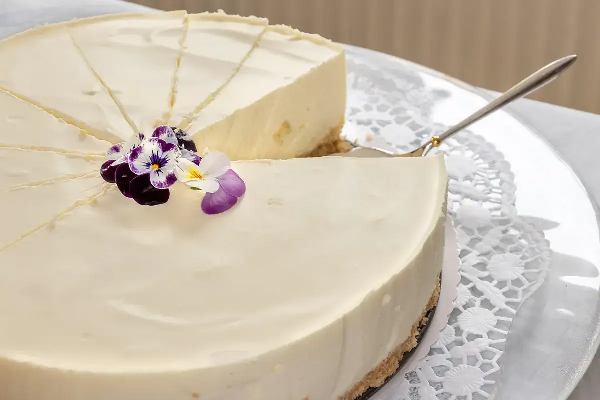 Cheesecake senza gelatina, cremosa e decorata con fiori viola e bianchi, pronta per essere gustata.