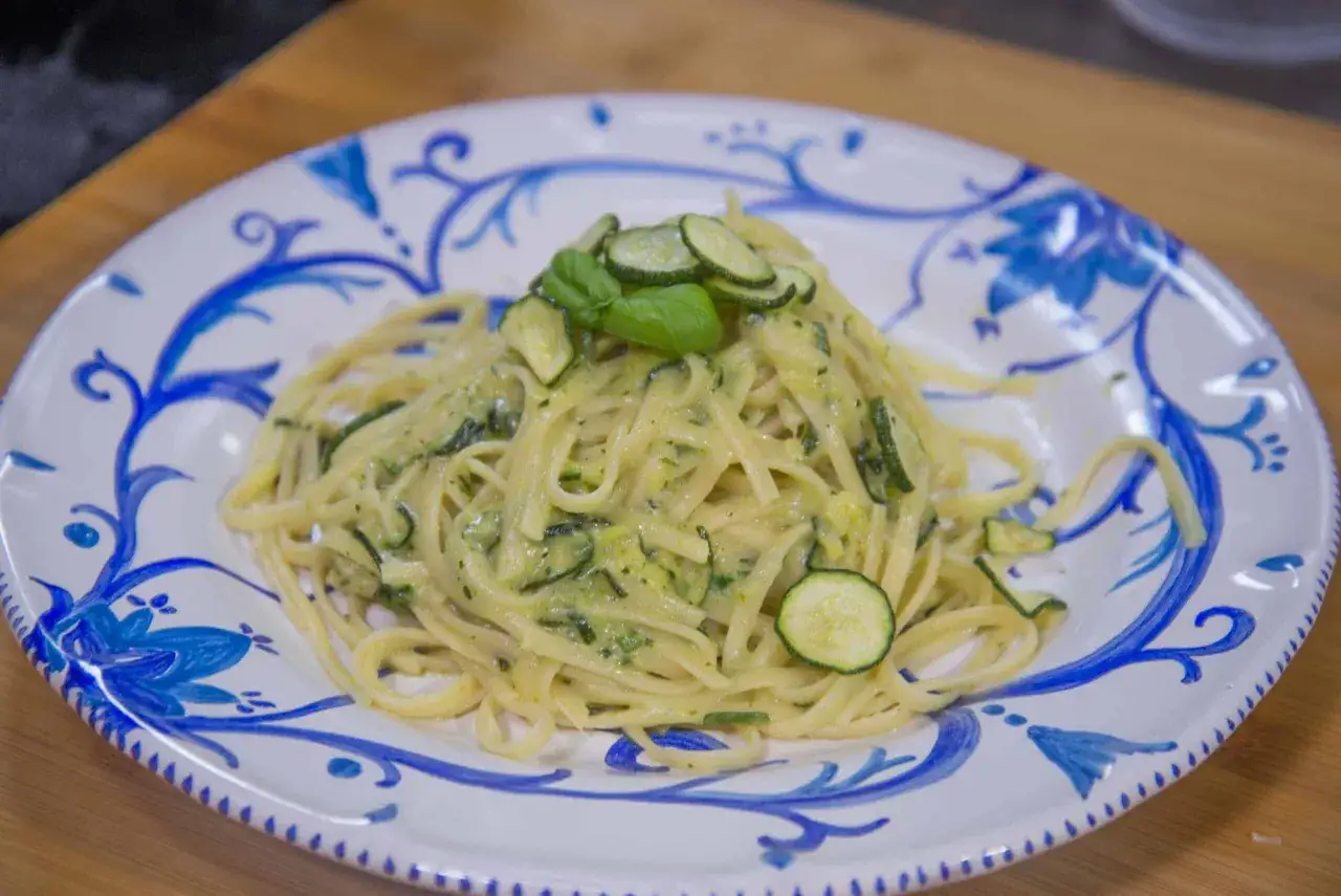 Spaghetti alla Nerano cremosi con zucchine fresche e basilico, serviti su un piatto decorato con motivi blu.