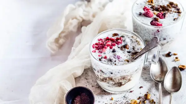Due bicchieri di yogurt con semi di chia, lamponi e granella di nocciole. Un dessert sano e gustoso.