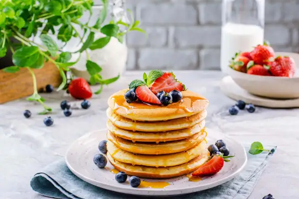 Pila di soffici pancake senza glutine, guarniti con fragole, mirtilli e sciroppo d'acero.