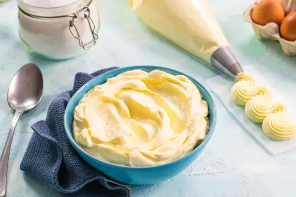 Una ciotola blu piena di soffice crema al mascarpone, pronta per decorare dolci. Accanto, sac à poche e uova.