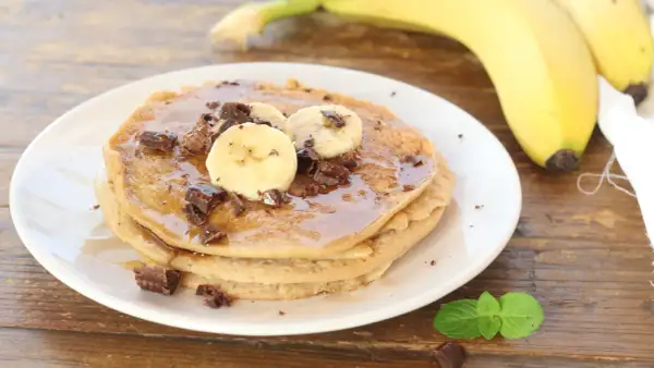 Pancake alla banana con scaglie di cioccolato e sciroppo d'acero, guarniti con fettine di banana fresca.