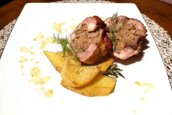 Coniglio in porchetta ripieno, servito con patate arrosto e salsa.