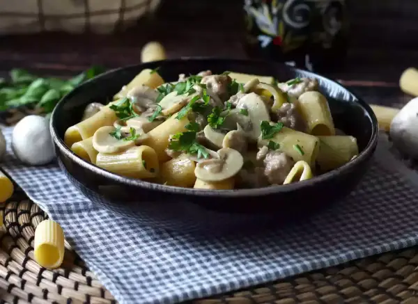 Piatto fumante di pasta con funghi e salsiccia, guarnito con prezzemolo fresco. Un classico confortante.