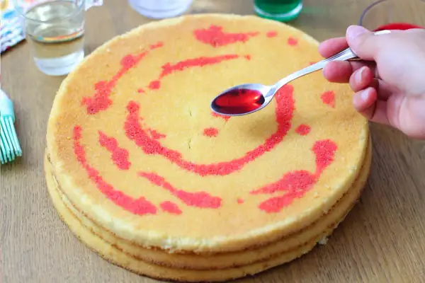 Mano versa sciroppo rosso su pan di spagna decorato.