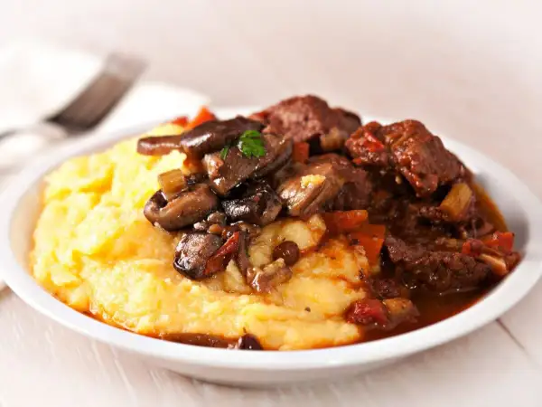 Polenta cremosa con spezzatino di manzo e funghi. Un classico piatto italiano, perfetto per scoprire polenta con cosa accompagnarla.