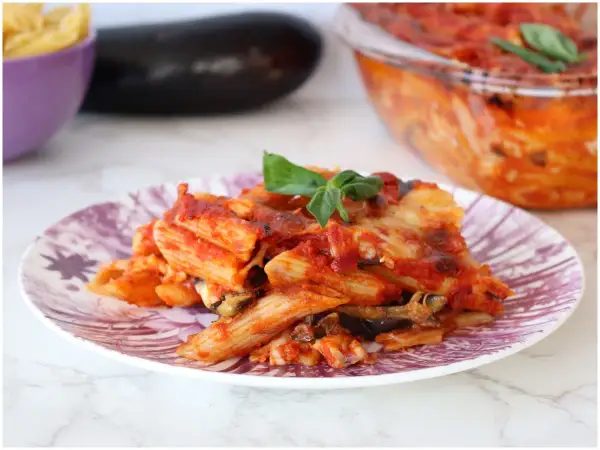 Piatto di pasta alla siciliana con melanzane, pomodoro e formaggio fuso, guarnito con basilico fresco.