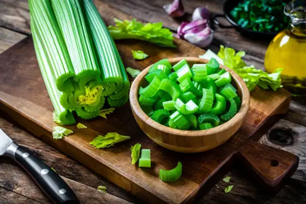 Fresh celery stalks and chopped celery in a wooden bowl on a cutting board.