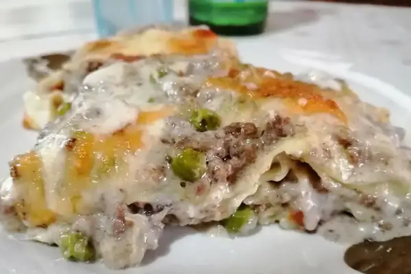 Porzione di lasagne bianche sfiziose con ragù, piselli e besciamella filante, gratinate al forno.