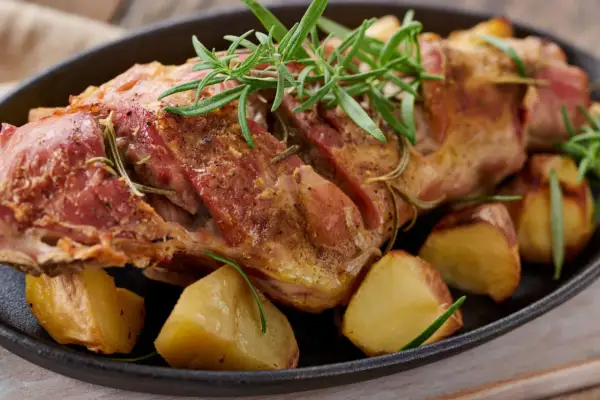 Succulento agnello al forno, dorato e profumato al rosmarino, servito con patate arrosto in una padella di ghisa.