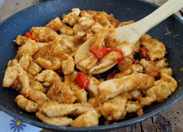 Straccetti di pollo dorati e saporiti in padella con pomodorini, pronti per essere gustati.