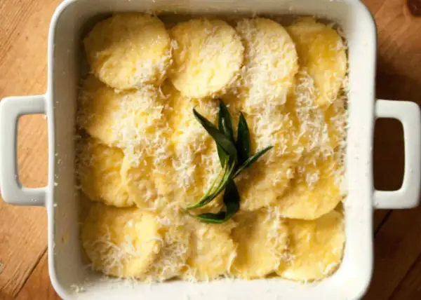 Gnocchi alla Romana pronti per essere infornati, conditi con parmigiano grattugiato e un rametto di salvia.