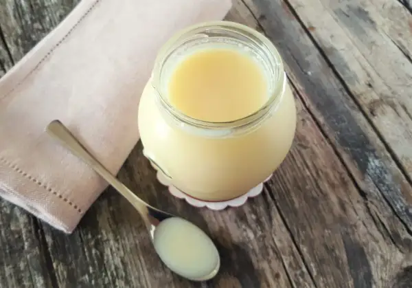 Un vasetto di latte condensato fatto in casa, denso e cremoso, pronto per dolci deliziosi. Un cucchiaino ne mostra la consistenza perfetta.