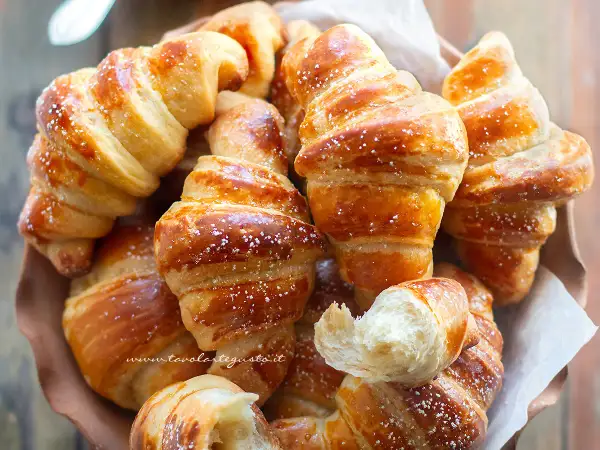 Cornetti fatti in casa dorati e soffici, spolverati di zucchero a velo, invitano a una colazione golosa.