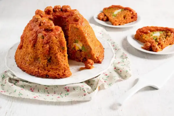 Sartu di riso, un tortino di riso rosso con polpettine e uova sode, servito su un piatto con tovagliolo fiorato.
