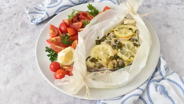 Delizioso pesce spada al forno in cartoccio con limone, capperi e prezzemolo, accompagnato da pomodorini freschi.
