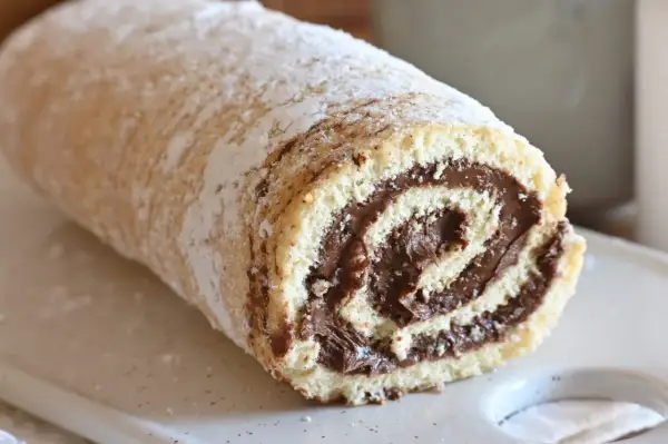 Un soffice rotolo alla Nutella, cosparso di zucchero a velo, pronto per essere gustato.