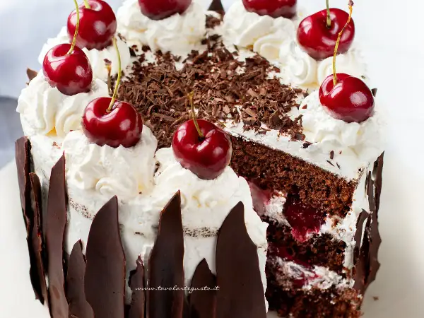 Una fetta di foresta nera torta, con panna montata, ciliegie fresche e riccioli di cioccolato.